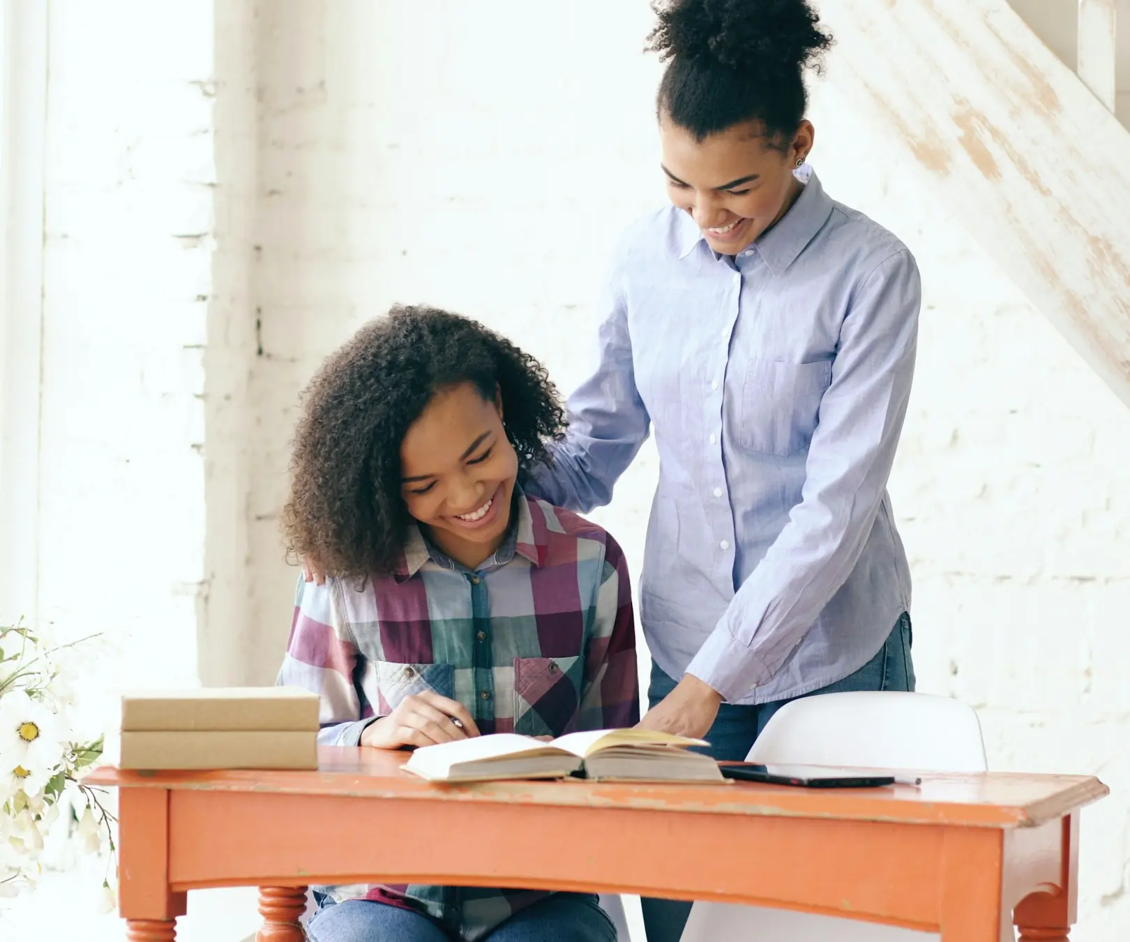 A tutor guiding a smiling student as she works through a book at her desk