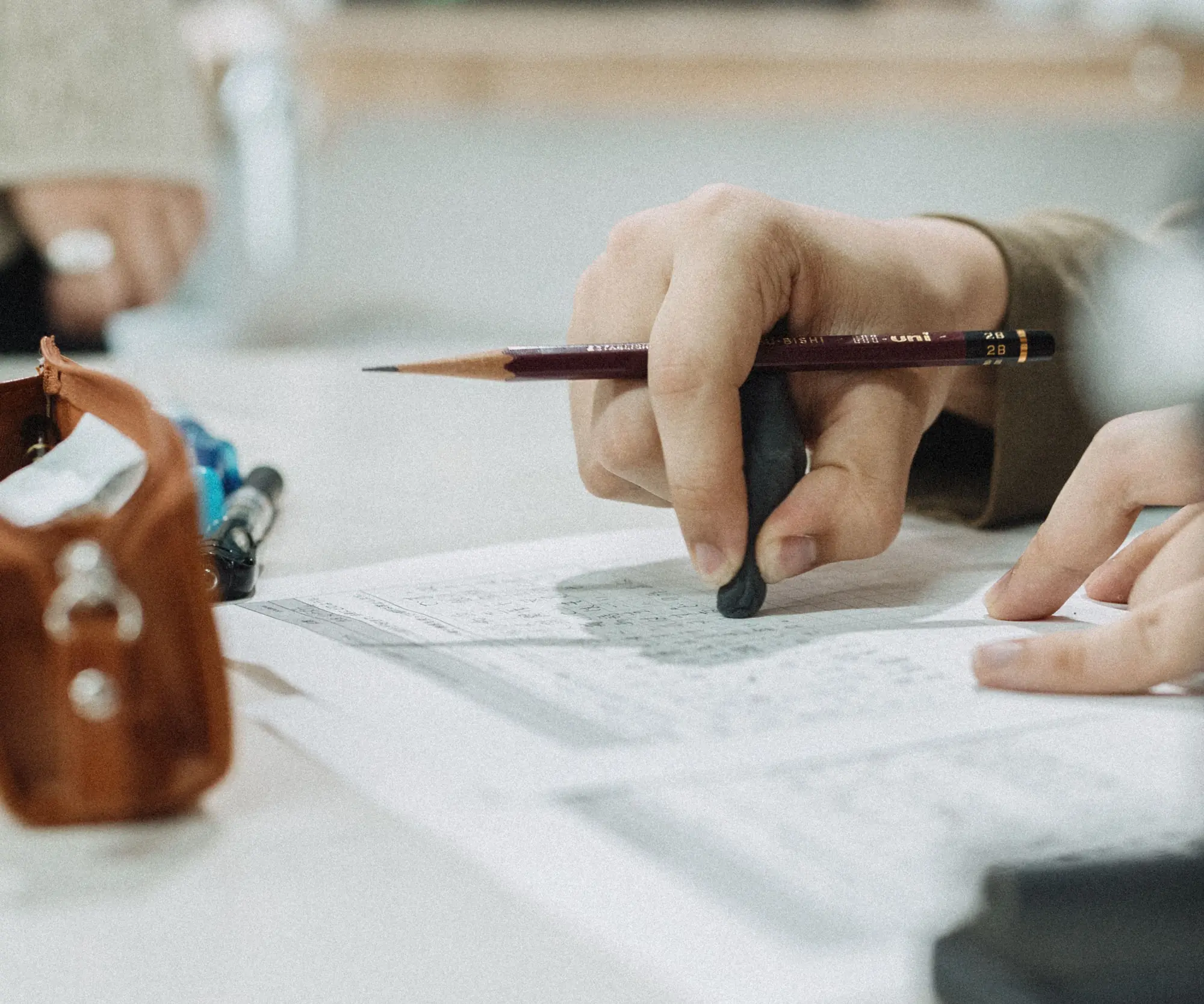 A student working through written exercises with a pencil and eraser at a study table